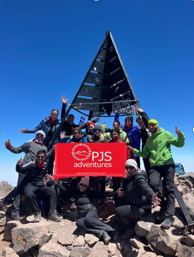 A group celebrating together at the summit marker of Mount Toubkal
